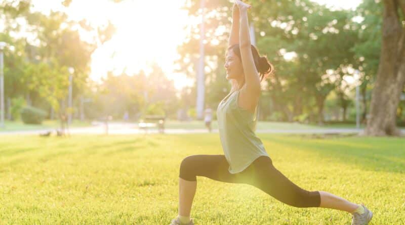 Weibliche Joggerin. Fit junge asiatische Frau in grüner Sportkleidung dehnt ihre Muskeln im Park vor dem Laufen und genießt die gesunde frische Luft im Freien.